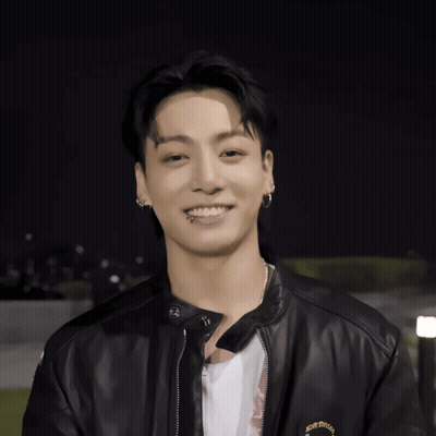 A Young Man Wearing A Black Leather Jacket And Earrings Smiles GIF