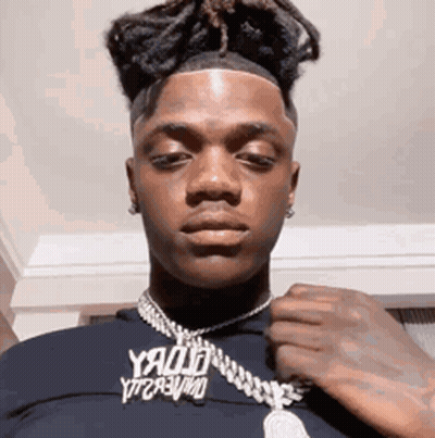 A Young Man Wearing A Black Shirt And A Necklace Is Looking At The Camera . GIF