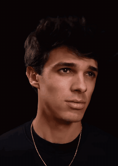 A Young Man Wearing A Black Shirt And Gold Chain Is Smiling GIF
