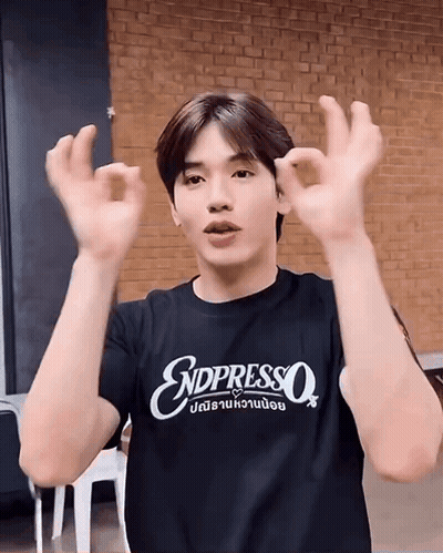A Young Man Wearing A Black T-Shirt That Says Endpresso Is Making An Ok Sign With His Hands . GIF