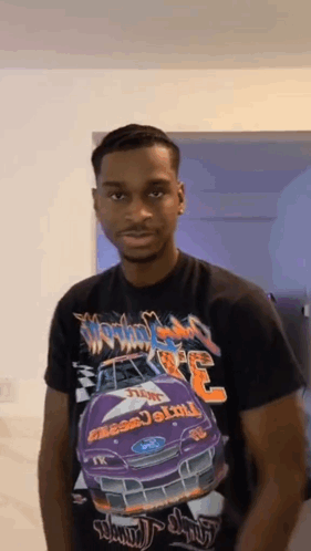A Young Man Wearing A Black T-Shirt With A Purple Race Car On It Is Standing In A Room . GIF