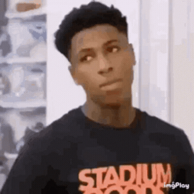 A Young Man Wearing A Black T-Shirt With The Word Stadium On It Is Standing In Front Of A Shoe Rack . GIF