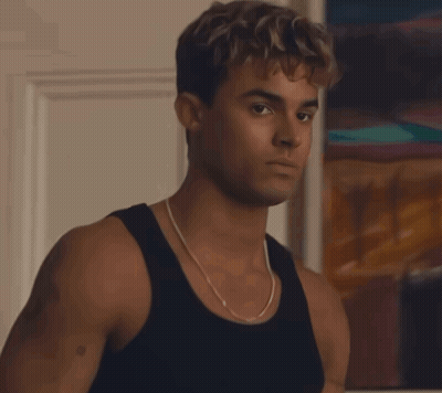A Young Man Wearing A Black Tank Top And A Chain Around His Neck Looks At The Camera GIF