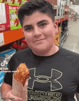 A Young Man Wearing A Black Under Armour Shirt Is Holding A Fried Chicken Wing In A Paper Bag . GIF