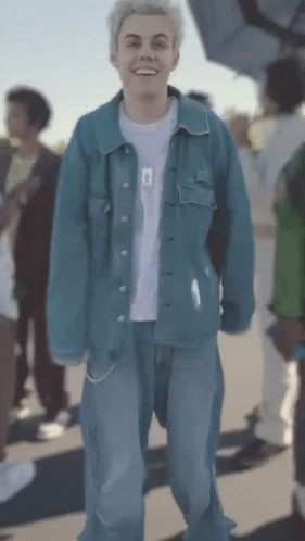 A Young Man Wearing A Blue Denim Jacket And Blue Jeans Is Smiling GIF