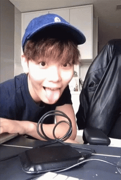 A Young Man Wearing A Blue Hat Is Sticking His Tongue Out While Sitting At A Desk . GIF