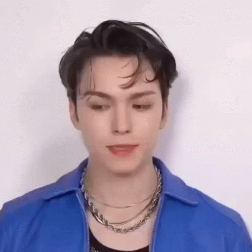 A Young Man Wearing A Blue Jacket And A Necklace Is Looking Down . GIF