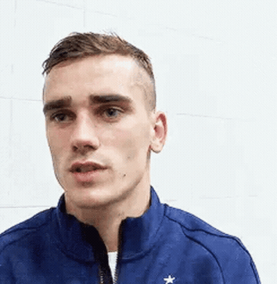 A Young Man Wearing A Blue Jacket With A Star On It Is Standing In Front Of A White Wall . GIF