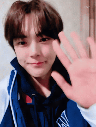 A Young Man Wearing A Blue Jacket With The Letter W On It Waves His Hand GIF