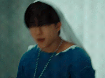 A Young Man Wearing A Blue Shirt And A White Veil Is Standing In Front Of A Window . GIF