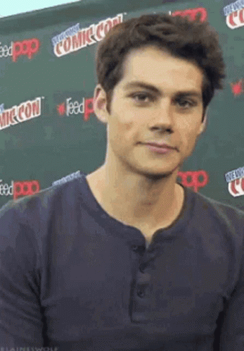A Young Man Wearing A Blue Shirt Is Standing In Front Of A Comic Con Sign . GIF