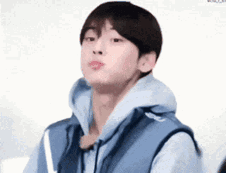 A Young Man Wearing A Blue Vest And A Hoodie Is Making A Face . GIF