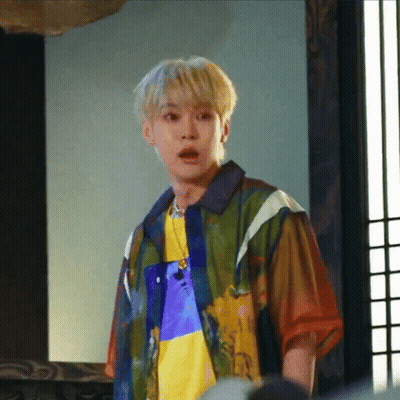 A Young Man Wearing A Colorful Shirt And A Necklace Is Standing In A Room . GIF