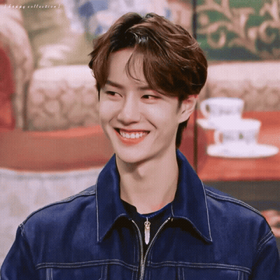 A Young Man Wearing A Denim Jacket Is Smiling In Front Of A Table With Coffee Cups And Saucers GIF