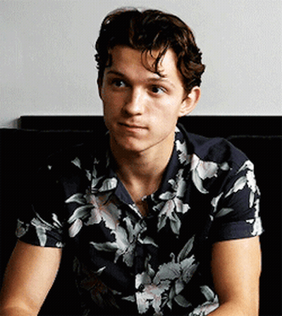 A Young Man Wearing A Floral Shirt Is Sitting On A Couch Looking At The Camera . GIF