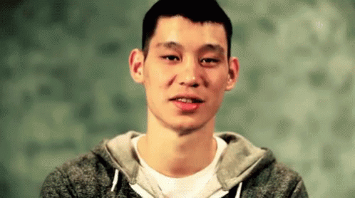 A Young Man Wearing A Gray Hoodie And A White Shirt Is Looking At The Camera . GIF