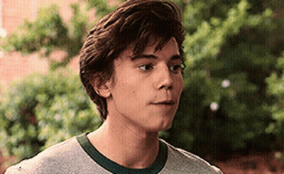 A Young Man Wearing A Gray T-Shirt And A Green Collar Is Looking At The Camera . GIF
