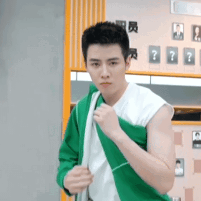 A Young Man Wearing A Green Jacket And A White Shirt Is Standing In A Gym . GIF