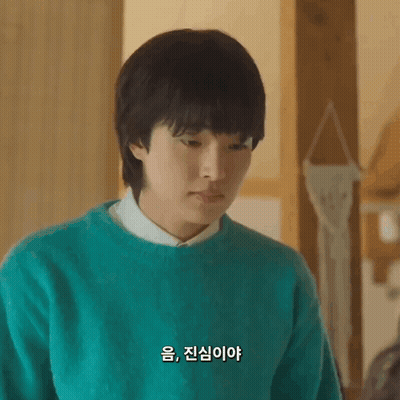A Young Man Wearing A Green Sweater And A White Shirt Is Looking Down . GIF