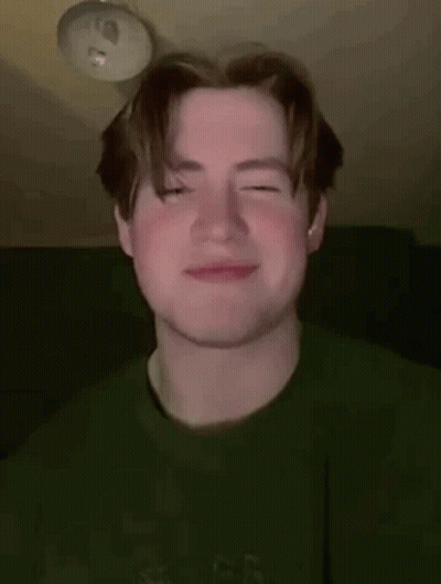 A Young Man Wearing A Green Sweater Is Smiling With His Eyes Closed . GIF