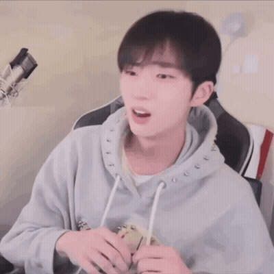 A Young Man Wearing A Grey Hoodie Is Sitting In Front Of A Microphone .. GIF