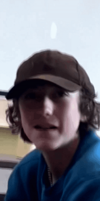 A Young Man Wearing A Hat And A Blue Shirt Is Making A Funny Face . GIF