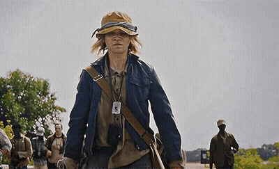 A Young Man Wearing A Hat And A Jacket Is Walking Down A Street . GIF