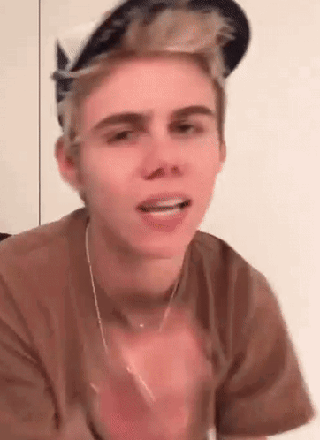 A Young Man Wearing A Hat And A Necklace Is Making A Face . GIF