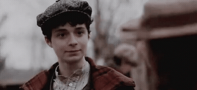 A Young Man Wearing A Hat And A Plaid Jacket Is Smiling . GIF