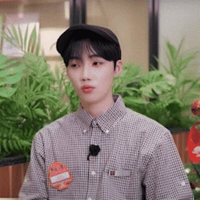 A Young Man Wearing A Hat And A Plaid Shirt Is Sitting In Front Of A Plant . GIF