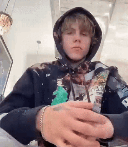A Young Man Wearing A Hoodie And A Bracelet Is Sitting At A Table With His Hands Folded . GIF