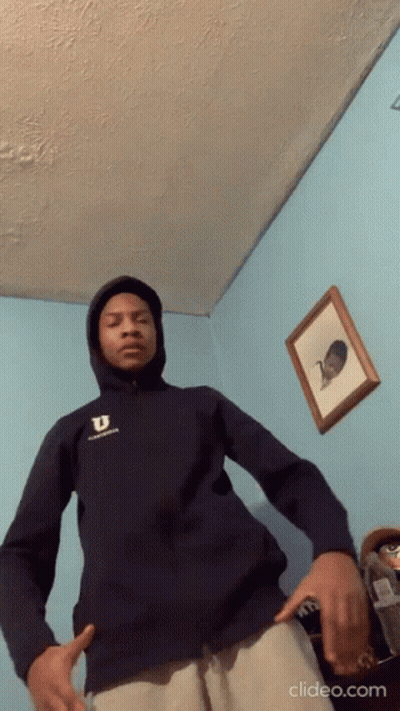 A Young Man Wearing A Hoodie Is Standing In A Room . GIF