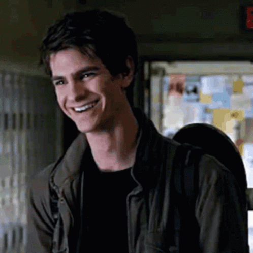 A Young Man Wearing A Jacket And A Backpack Is Smiling In A Room . GIF