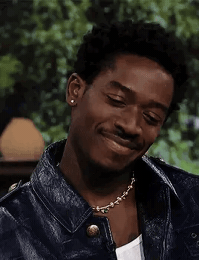 A Young Man Wearing A Leather Jacket And A Necklace Is Smiling . GIF