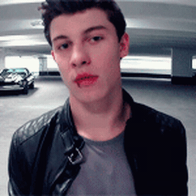A Young Man Wearing A Leather Jacket Is Standing In A Parking Garage Looking At The Camera . GIF