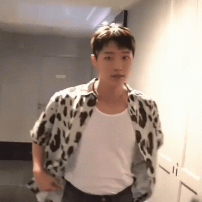 A Young Man Wearing A Leopard Print Shirt Is Standing In A Hallway . GIF