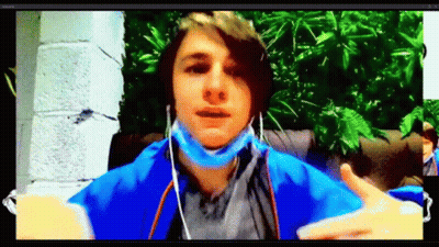 A Young Man Wearing A Mask And Ear Buds Is Sitting In Front Of A Computer Screen . GIF