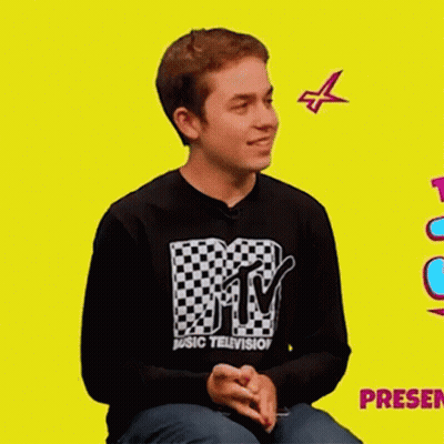 A Young Man Wearing A Mtv Music Television Shirt Is Sitting On A Yellow Background . GIF