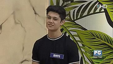 A Young Man Wearing A Name Tag With The Name Rhys On It GIF