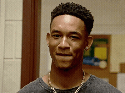 A Young Man Wearing A Necklace And Earrings Is Smiling . GIF