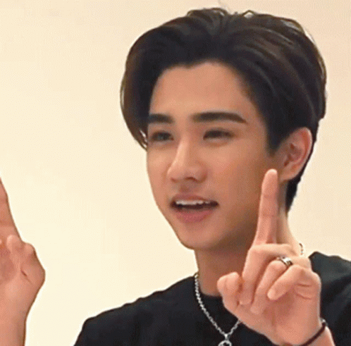A Young Man Wearing A Necklace With The Letter C On It Is Pointing Up GIF