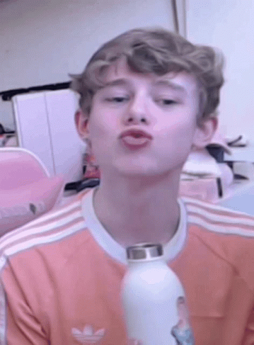 A Young Man Wearing A Pink Adidas Shirt Is Holding A White Water Bottle . GIF