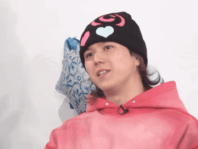 A Young Man Wearing A Pink Hoodie And A Black Beanie With Hearts On It GIF