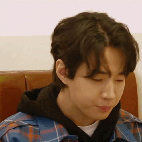 A Young Man Wearing A Plaid Shirt And A Black Hoodie Is Sitting In A Chair . GIF