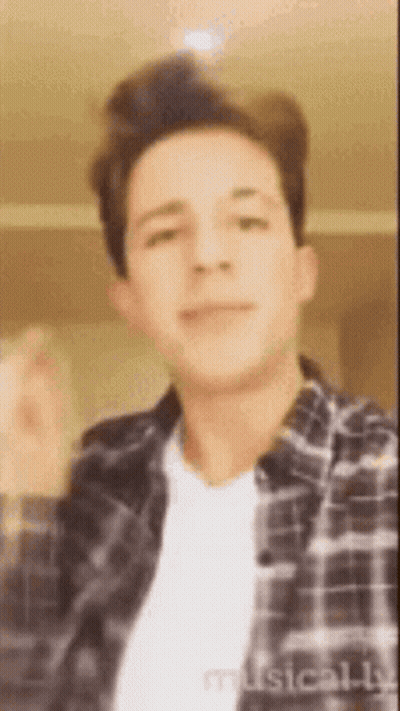 A Young Man Wearing A Plaid Shirt And A White T-Shirt Is Making A Funny Face . GIF