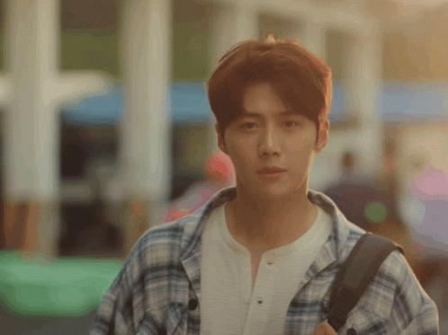 A Young Man Wearing A Plaid Shirt And Carrying A Backpack Looks At The Camera GIF
