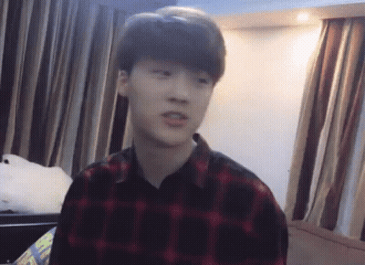 A Young Man Wearing A Plaid Shirt Is Sitting In A Room With Curtains . GIF