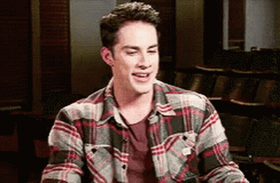 A Young Man Wearing A Plaid Shirt Is Smiling In A Classroom . GIF