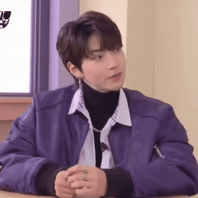 A Young Man Wearing A Purple Jacket And A Turtleneck Is Sitting At A Table . GIF