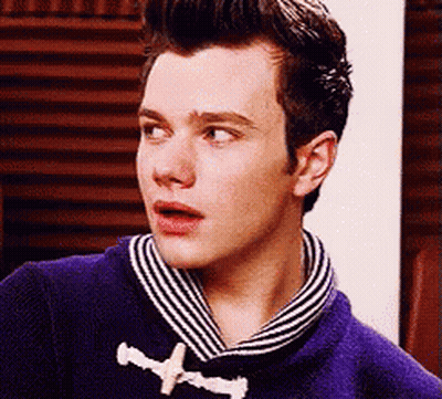 A Young Man Wearing A Purple Sweater And A Striped Scarf Looks At The Camera . GIF